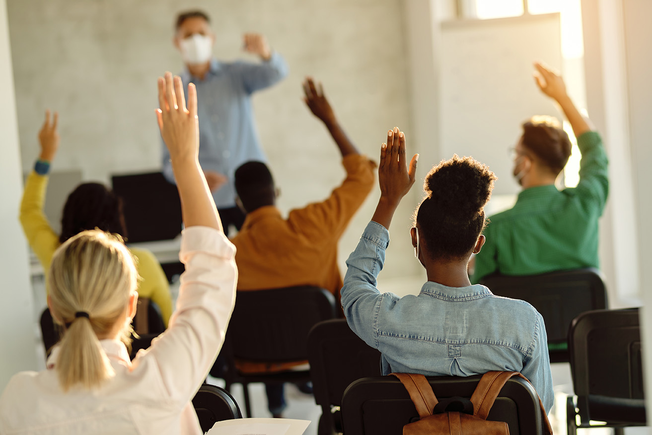 People raising hands in class wearing masks